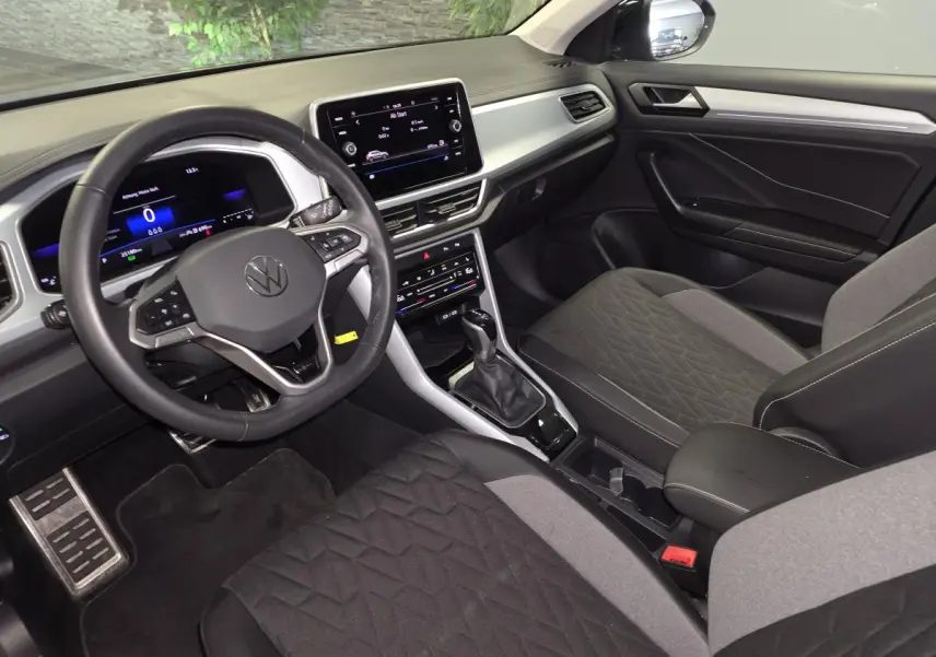 Vue intérieure côté conducteur du Volkswagen T-Roc gris 2025, avec tableau de bord digital et volant multifonction cuir.