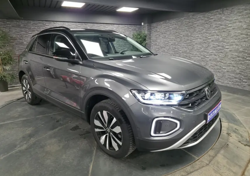 Volkswagen T-Roc gris 3/4 avant droit en intérieur, avec phares LED allumés et jantes alliage 17 pouces.