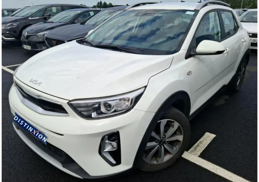 KIA Stonic blanc vue 3/4 avant droit, SUV compact avec toit noir et jantes alliage, stationné sur parking.