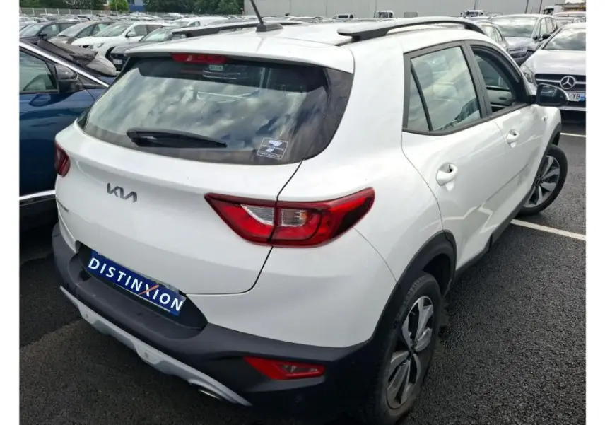 Vue 3/4 arrière droite d'un Kia Stonic blanc 2022 avec feux arrière rouges et toit avec barres de toit noires.