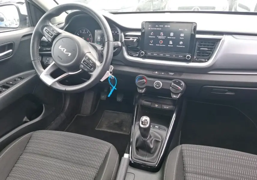 Vue intérieure avant du Kia Stonic blanc 2022, avec volant multifonction, écran tactile et levier de vitesses manuel.