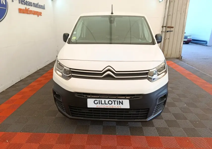 Vue de face d’un Citroën Berlingo blanc avec pare-chocs noir et phares allumés dans un garage.