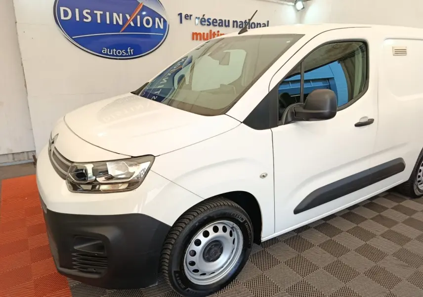 Vue 3/4 avant droit d’un Citroën Berlingo blanc utilitaire avec pare-chocs noir et jantes acier en showroom.