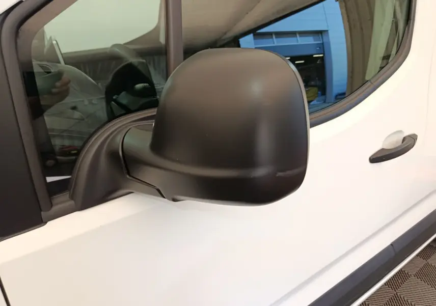 Rétroviseur noir côté conducteur d’un Citroën Berlingo blanc, vue rapprochée sur la portière avant gauche.