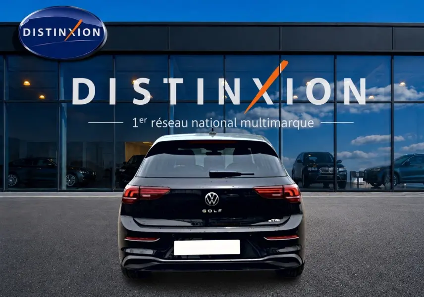 Vue arrière d'une Volkswagen Golf noire 2026 garée devant une vitrine avec logo Distinxion.
