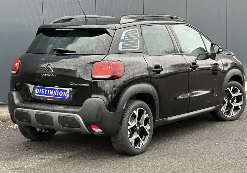 Vue 3/4 arrière droit d'une Citroën C3 Aircross 2024 noir Perla avec jantes alliage et barres de toit.