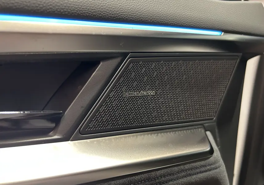 Gros plan sur la porte côté gauche du Renault Austral blanc nacré, mettant en valeur l'enceinte Harman Kardon et l'éclairage d'ambiance bleu.