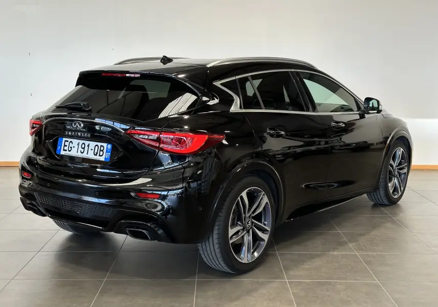 Vue 3/4 arrière droite d'une Infiniti Q30 noire 2016 avec jantes alliage et vitres teintées en intérieur showroom.