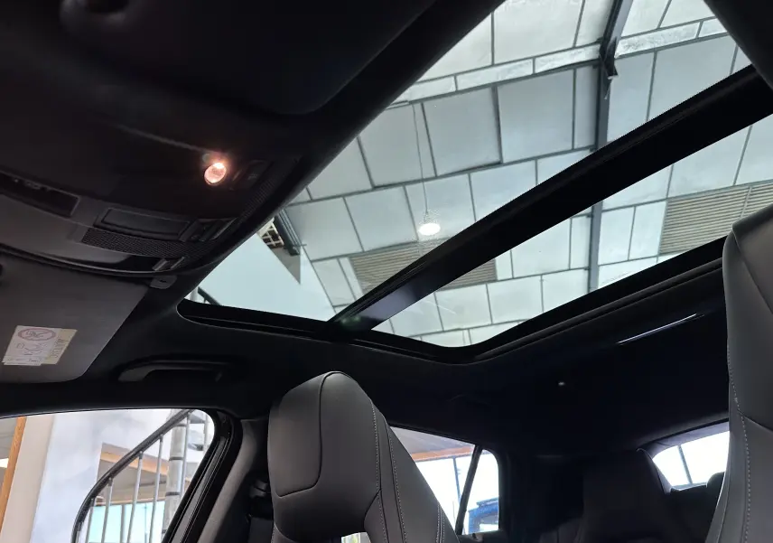 Toit panoramique ouvert vu de l'intérieur sur une INFINITI Q30 noire, avec sièges avant en cuir et ambiance sombre.