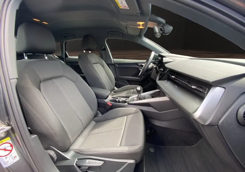 Vue intérieure côté conducteur de l'Audi A3 Sportback 30 TFSI 2021 avec sièges tissu noir et tableau de bord moderne.