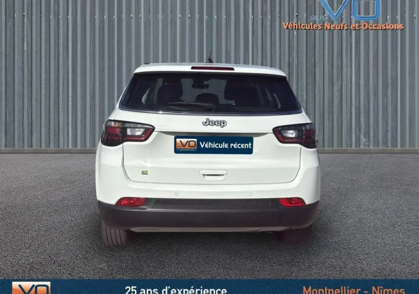 Vue arrière d'un Jeep Compass blanc 2024 avec feux arrière sombres et logo Jeep visible sur un sol gris.