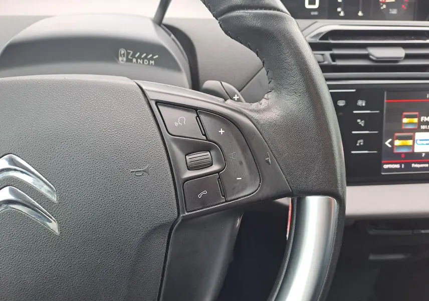 Gros plan sur le volant noir de la Citroën C4 Spacetourer 2018 avec commandes audio et tableau de bord numérique en arrière-plan.