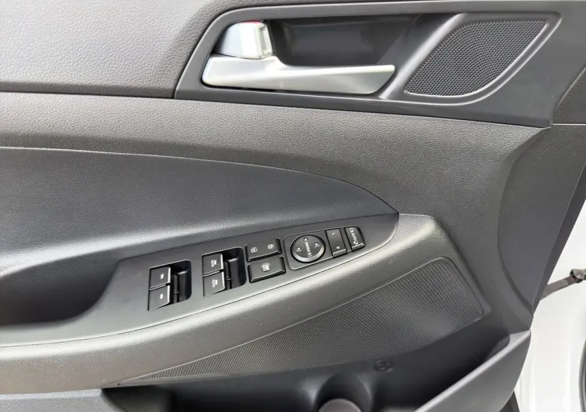 Vue rapprochée de la porte avant gauche du Hyundai Tucson blanc polar, avec commandes électriques et poignée argentée.