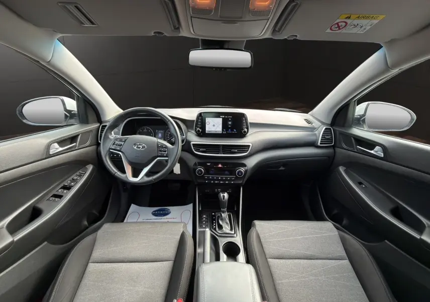 Vue intérieure avant du Hyundai Tucson 2020, tableau de bord et sièges tissu noir avec console centrale et écran tactile.