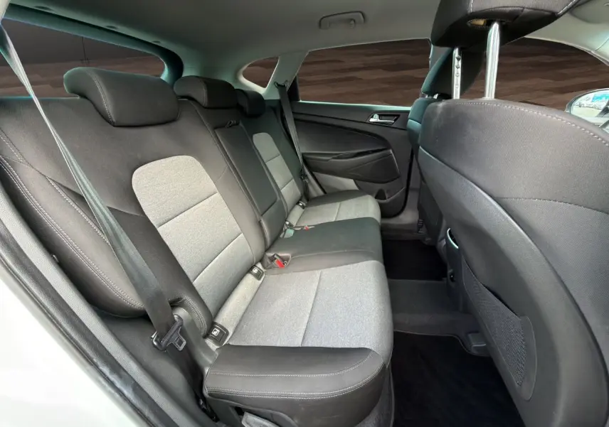 Vue intérieure arrière côté gauche du Hyundai Tucson blanc polar 2020, sièges tissu noir et gris avec ceintures de sécurité visibles.