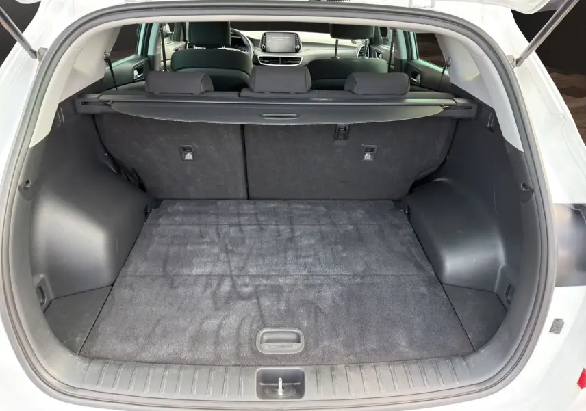Coffre ouvert du Hyundai Tucson blanc polar 2020, vue arrière montrant l'espace de chargement et la banquette arrière noire.
