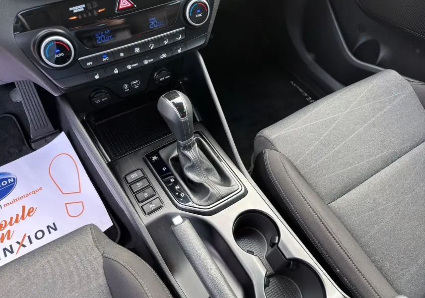 Vue intérieure centrée sur la console centrale du Hyundai Tucson 2020, avec levier de vitesse automatique et sièges tissu gris.