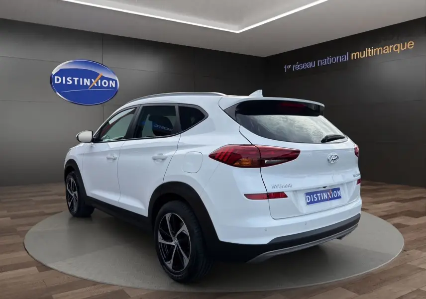 Vue 3/4 arrière droite du Hyundai Tucson blanc polar 2020 avec jantes 18 pouces bicolores dans un showroom.