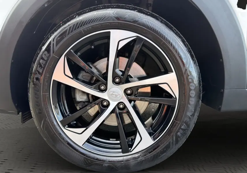 Gros plan sur la jante 18 pouces bicolore noire et argent d’un Hyundai Tucson blanc polar avec pneu Goodyear.