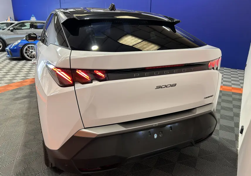 Vue 3/4 arrière droite du Peugeot 3008 blanc Okenite avec feux LED allumés et hayon électrique en intérieur showroom.