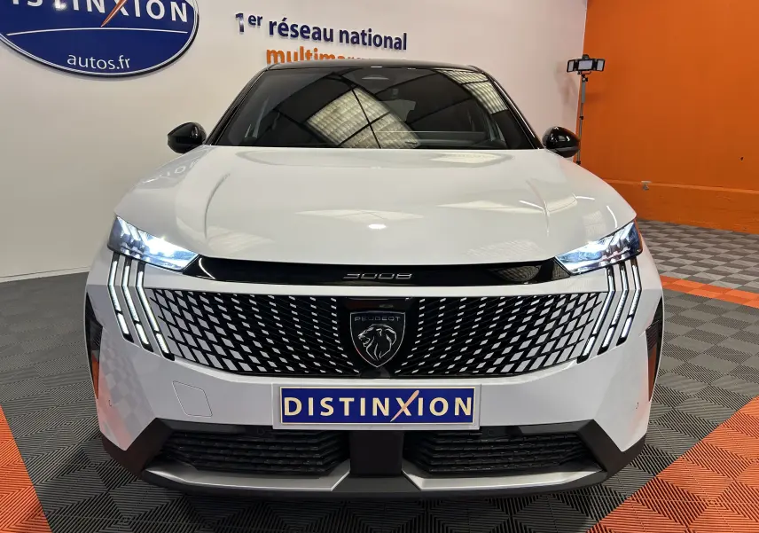 Vue frontale d'un Peugeot 3008 III Hybrid blanc Okenite avec calandre noire et phares LED allumés dans un showroom.