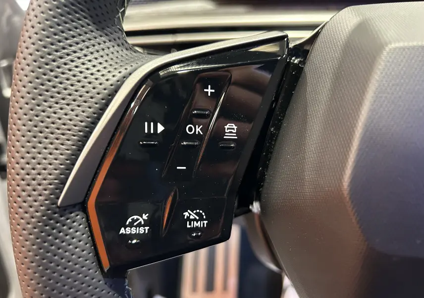 Gros plan sur les commandes noires du volant perforé du Peugeot 3008 blanc Okenite, version hybride 2025.