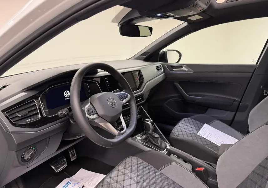 Vue intérieure côté conducteur du Volkswagen Taigo blanc pur, avec tableau de bord digital et sièges tissu gris à motifs.