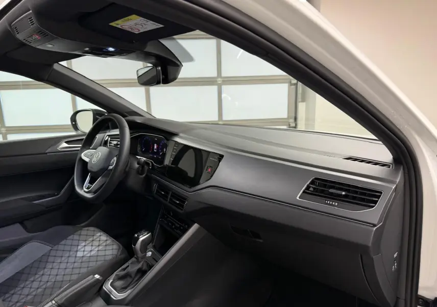 Vue intérieure côté conducteur du Volkswagen Taigo blanc pur, tableau de bord noir avec écran tactile et volant cuir multifonctions.