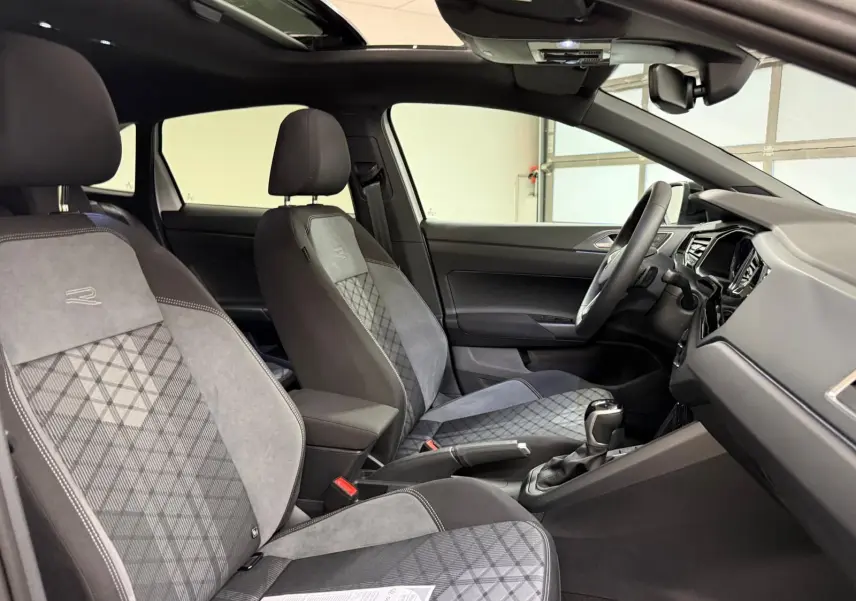 Vue intérieure côté conducteur du Volkswagen Taigo R-Line 2025, sièges sport gris avec surpiqûres et toit ouvrant noir visible.