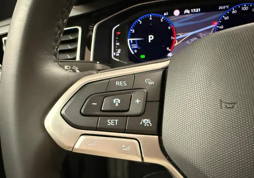 Gros plan sur les commandes multifonctions à gauche du volant cuir du Volkswagen Taigo blanc, affichage digital en arrière-plan.