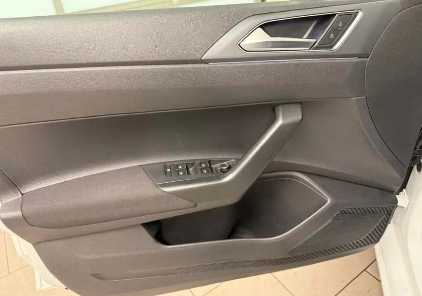 Vue rapprochée de la porte avant gauche du Volkswagen Taigo blanc pur, montrant les commandes de vitres et la poignée intérieure grise.