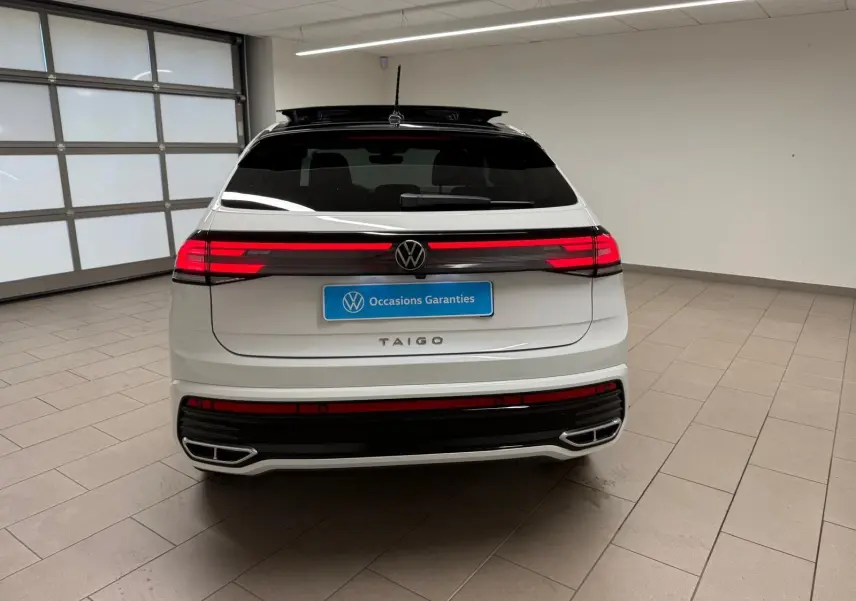 Vue arrière d'un Volkswagen Taigo blanc pur avec toit noir et feux arrière LED allumés en intérieur.