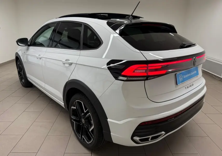 Vue 3/4 arrière droite du Volkswagen Taigo blanc pur avec toit noir et feux arrière LED allumés en intérieur.