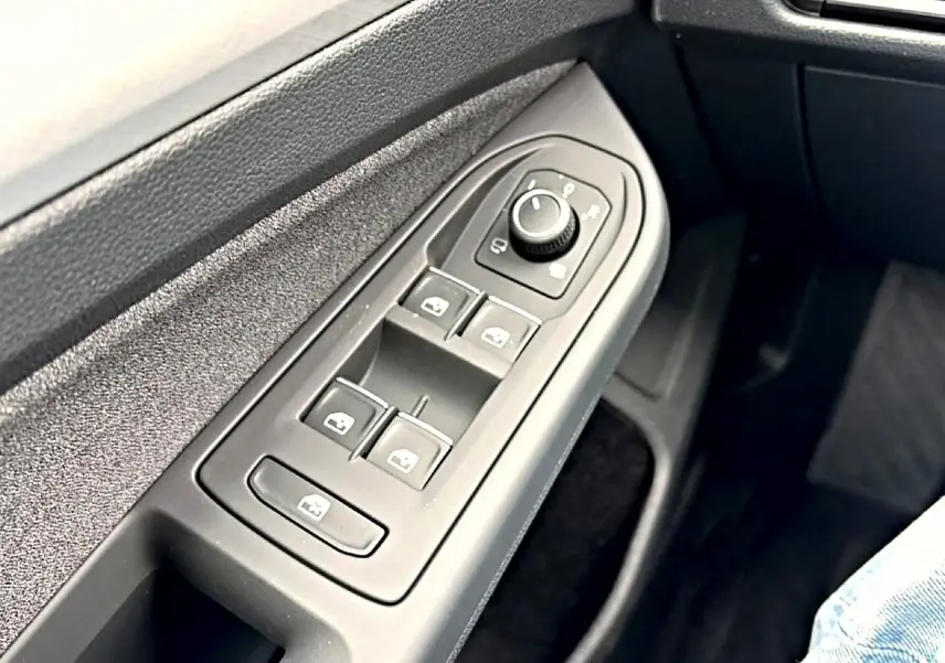 Gros plan sur les commandes des vitres et rétroviseurs côté conducteur d'une Volkswagen Golf bleu glacier.