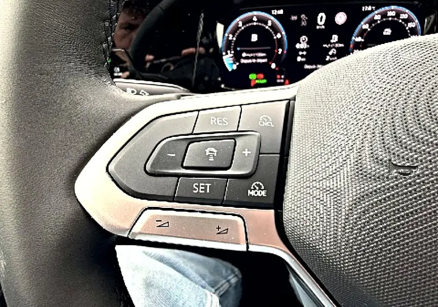 Gros plan sur le volant noir de la Volkswagen Golf 2026, avec commandes de régulateur de vitesse et tableau de bord numérique en arrière-plan.