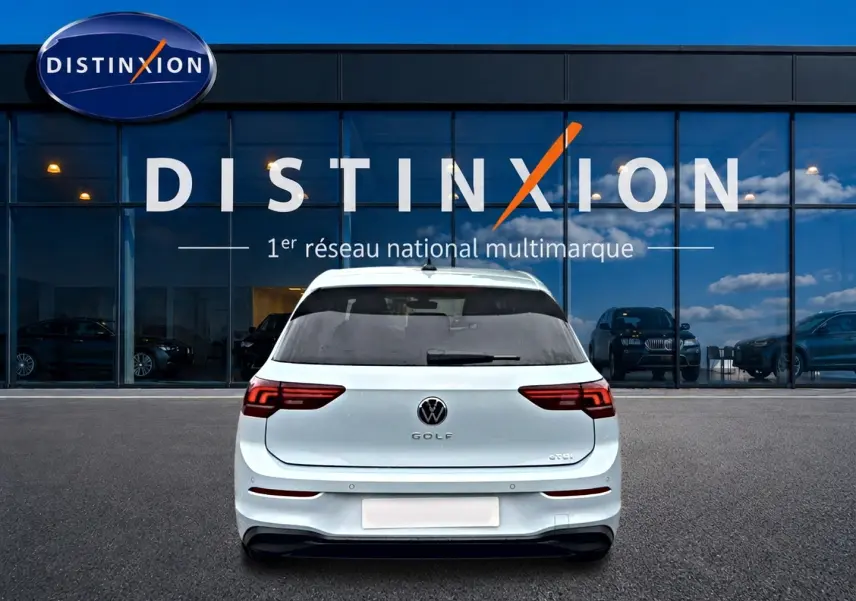 Vue arrière d'une Volkswagen Golf blanche stationnée devant une vitrine avec logo Distinxion visible.