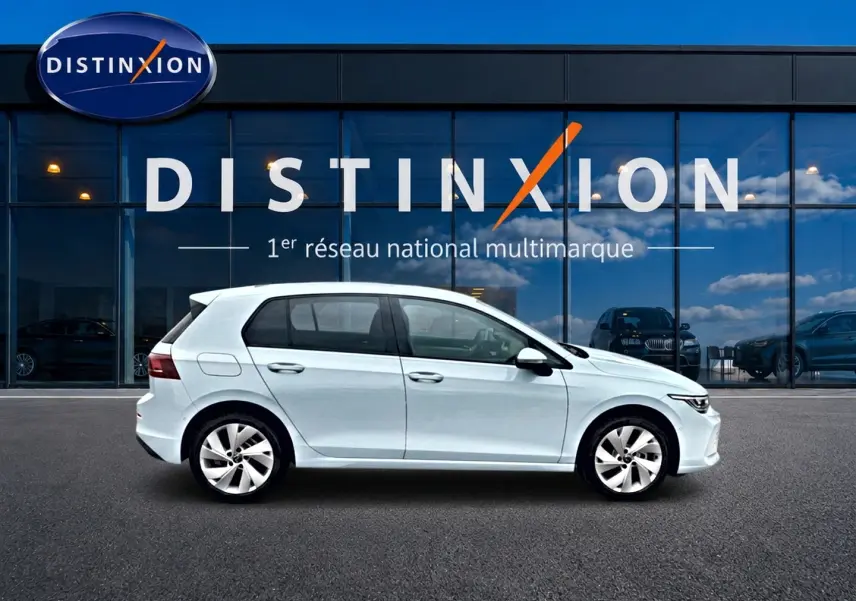 Vue de profil côté gauche d'une Volkswagen Golf 2026 bleu glacier garée devant une vitrine avec logo Distinxion.