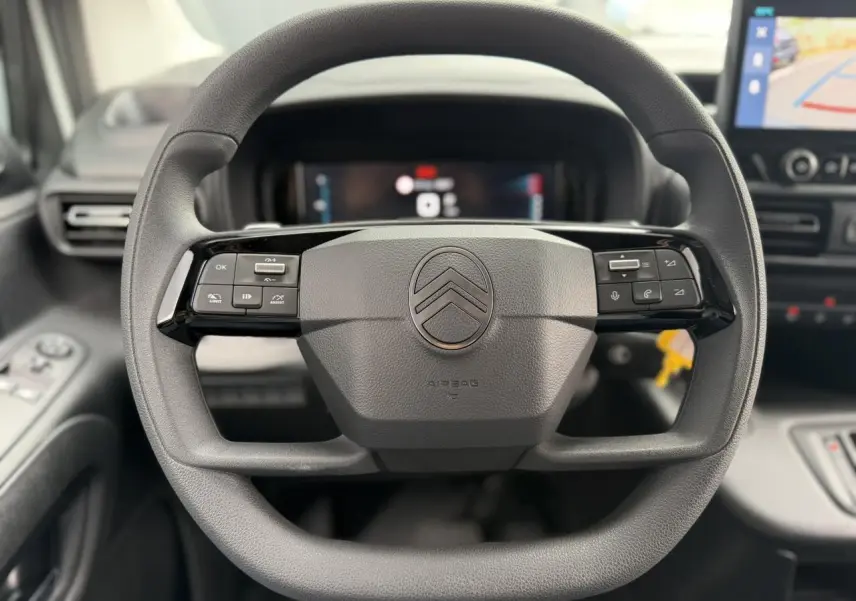 Vue rapprochée du volant multifonctions noir du Citroën Berlingo 2026 avec tableau de bord numérique en arrière-plan.