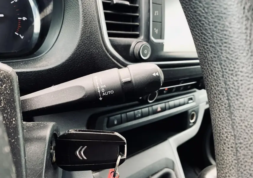 Vue rapprochée du tableau de bord et clé de contact du Citroën Jumpy XL blanc, avec commandes et volant partiellement visibles.