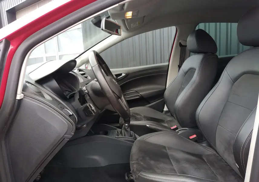 Vue intérieure côté conducteur d'une SEAT Ibiza ST rouge, mettant en valeur les sièges en cuir et alcantara noirs et le volant.