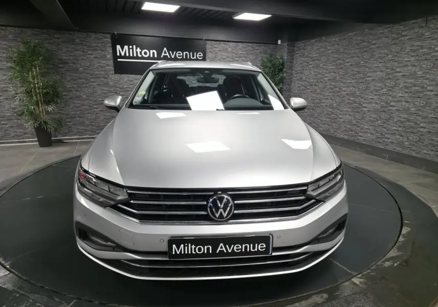 Volkswagen Passat SW gris métallisé vue de face dans un showroom avec logo VW et plaque Milton Avenue.