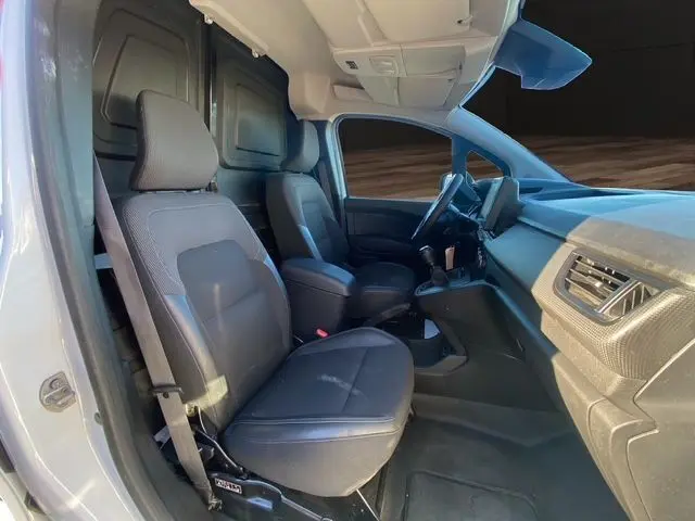 Vue intérieure côté gauche du Renault Kangoo Van TCE 100 blanc, montrant les sièges avant en tissu noir et le tableau de bord.