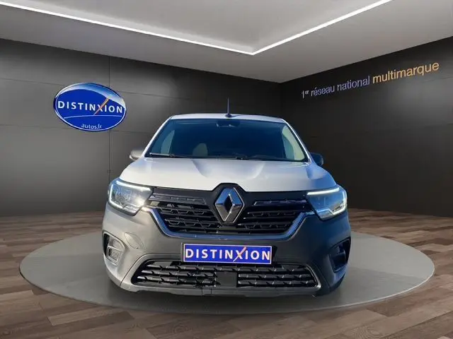 Vue frontale d'un Renault Kangoo blanc 2023 avec calandre noire et logo Renault proéminent, en showroom.