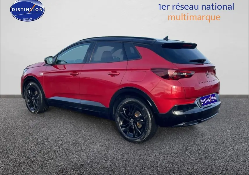Vue 3/4 arrière droite d’un Opel Grandland rouge avec toit noir et jantes noires, sur fond neutre.