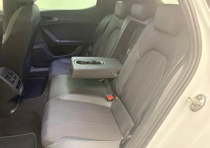 Vue intérieure côté droit des sièges arrière noirs avec accoudoir central et porte ouverte d'une CUPRA Leon blanche Nevada 2024.