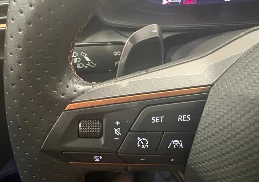 Gros plan sur les commandes du volant à gauche de la CUPRA Leon 2024, avec boutons de régulateur de vitesse et assistance à la conduite.