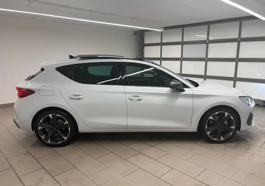 Vue de profil côté gauche d'une CUPRA Leon blanche Nevada avec toit ouvrant panoramique dans un garage.