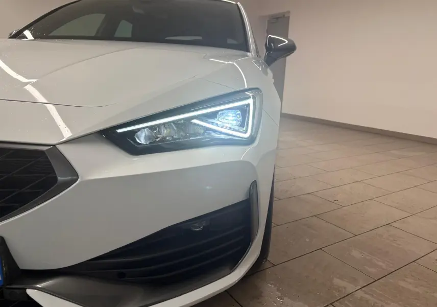 Gros plan sur l'avant droit de la CUPRA Leon blanche Nevada avec phare LED allumé et calandre noire.