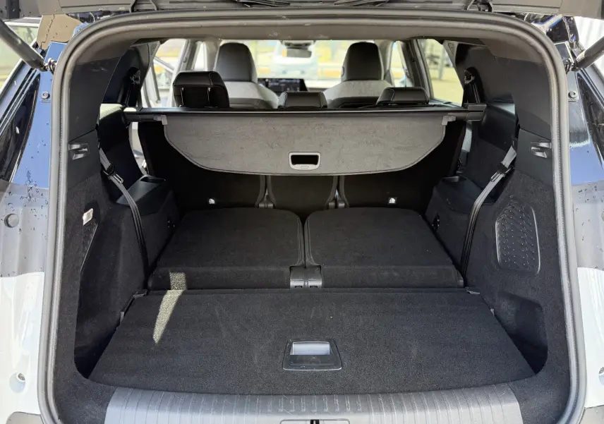 Coffre ouvert vu de l'arrière d'un Peugeot 5008 blanc Okenite avec banquette arrière rabattue et cache-bagages déployé.