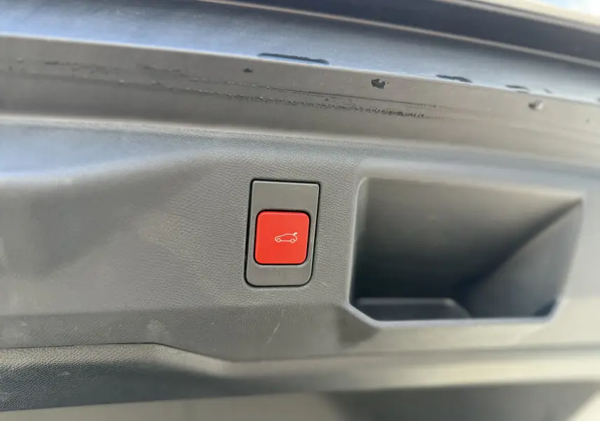 Gros plan sur le bouton rouge d'ouverture électrique du hayon dans l'intérieur du coffre du Peugeot 5008 blanc toit noir.